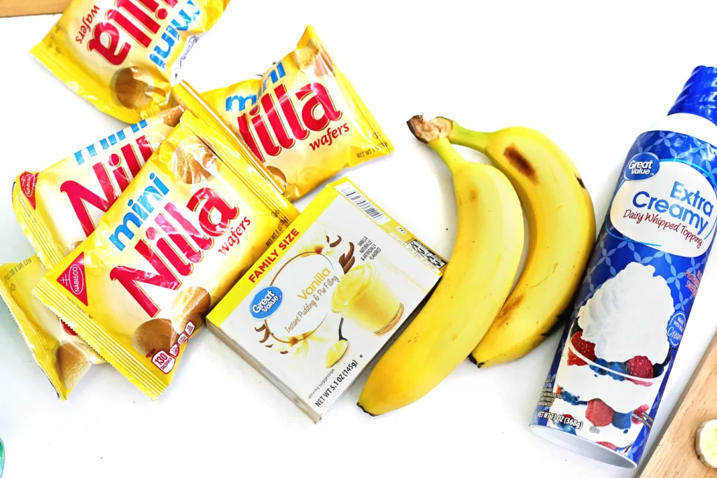 ingredients for the walking banana pudding recipe -multiple yellow Nabisco Nilla wafer packets, a bunch of bananas, and a blue-labeled bottle of dairy topping.