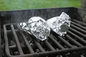 Aluminum foil covering waffle cones resting on charcoal grill grates.