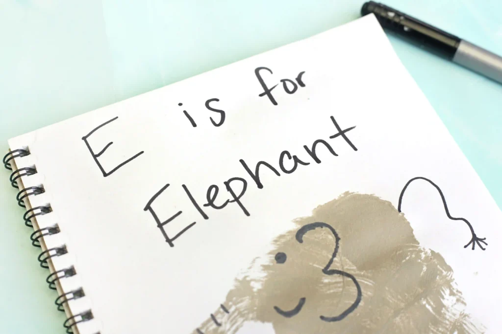 Letter E Elephant Handprint Craft - Cultivating Brilliant Minds an animal craft for kids that is a Notebook page with the handwritten phrase'E is for Elephant' and a gray handprint decorated to look like an elephant
