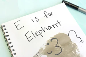 an animal craft for kids that is a Notebook page with the handwritten phrase 'E is for Elephant' and a gray handprint decorated to look like an elephant