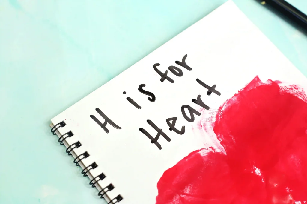 a notebook with a handprint heart that reads "H is for heart" for this alphabet craft for kids