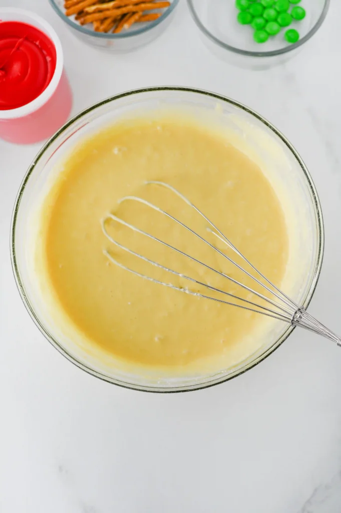 Apple Cupcakes - Cultivating Brilliant Minds Top-down view of a whisk mixing yellow batter in a glass bowl, with snacks and a red container nearby for these teacher appreciation gifts
