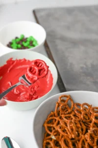 Close-up of a red pretzel-shaped candy on a fork over bowls of orange pretzels and colorful candies in the background for this teacher appreciation gift