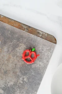 A pretzel dipped in red melted chocolate with a green and brown M&M