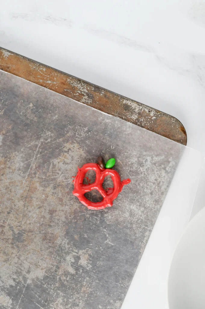 A pretzel dipped in red melted chocolate with a green and brown M&M