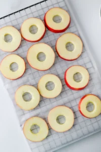 Red-skinned apple rings with hollow centers laid out on a parchment-lined baking sheet.