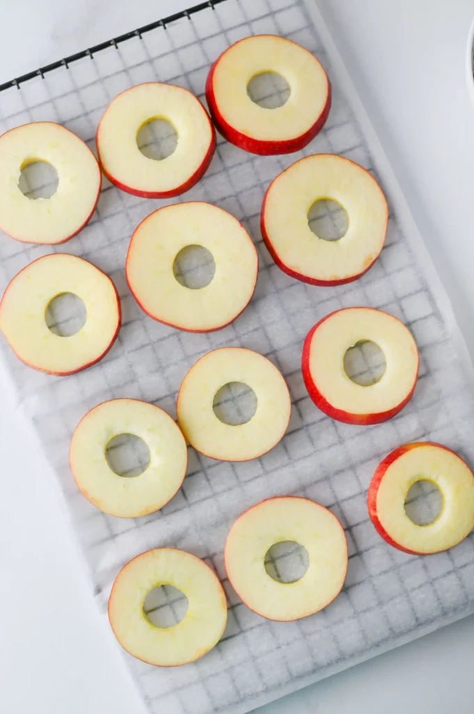 Red-skinned apple rings with hollow centers laid out on a parchment-lined baking sheet.