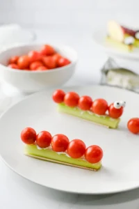 cherry tomatoes skewered on a green celery with cream cheese, arranged on a white plate.