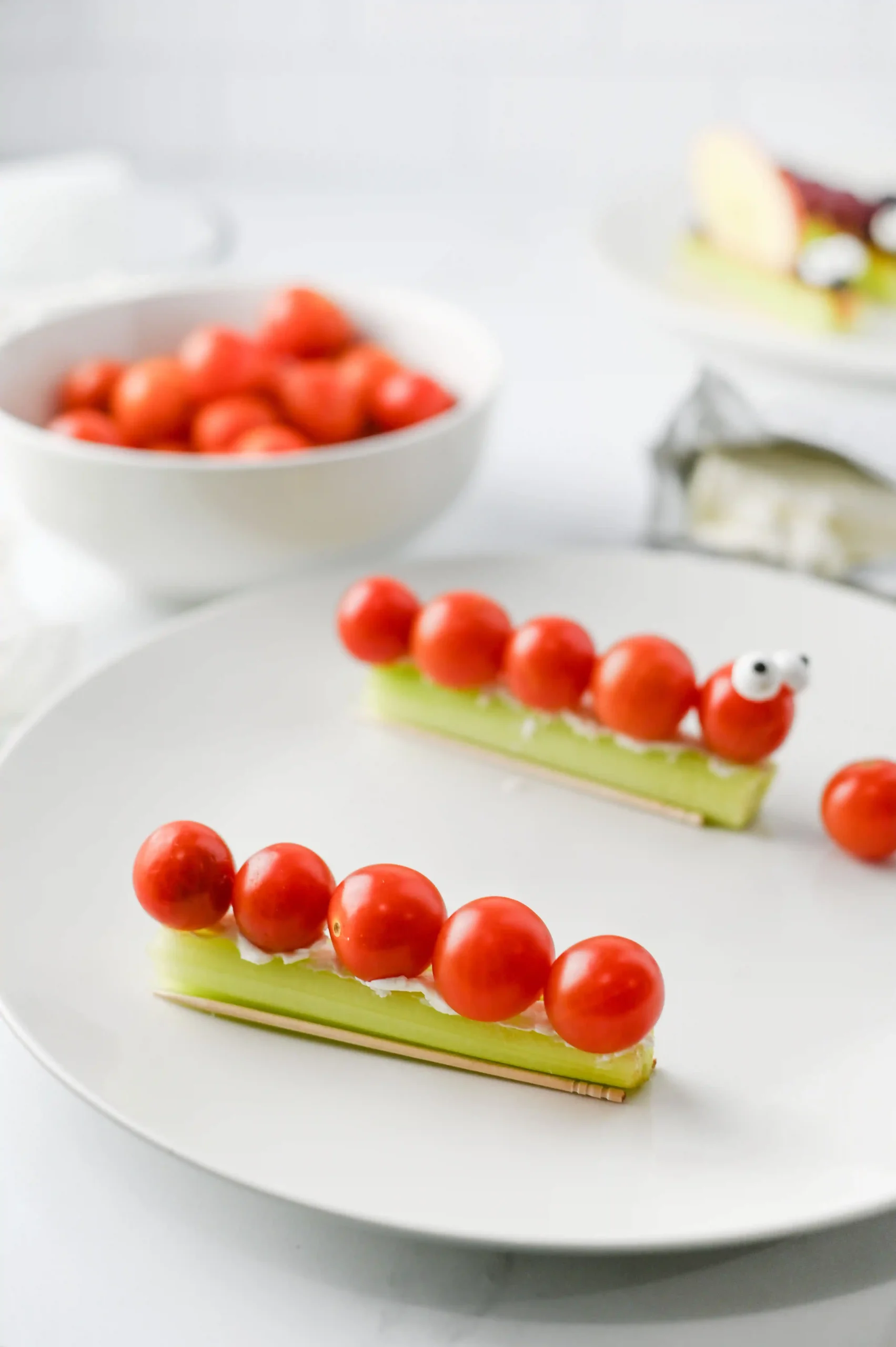 cherry tomatoes skewered on a green celery with cream cheese, arranged on a white plate.