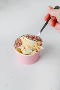 dot cakes in a paper cup with nonpareil sprinkles on top and a spoon scooping some out