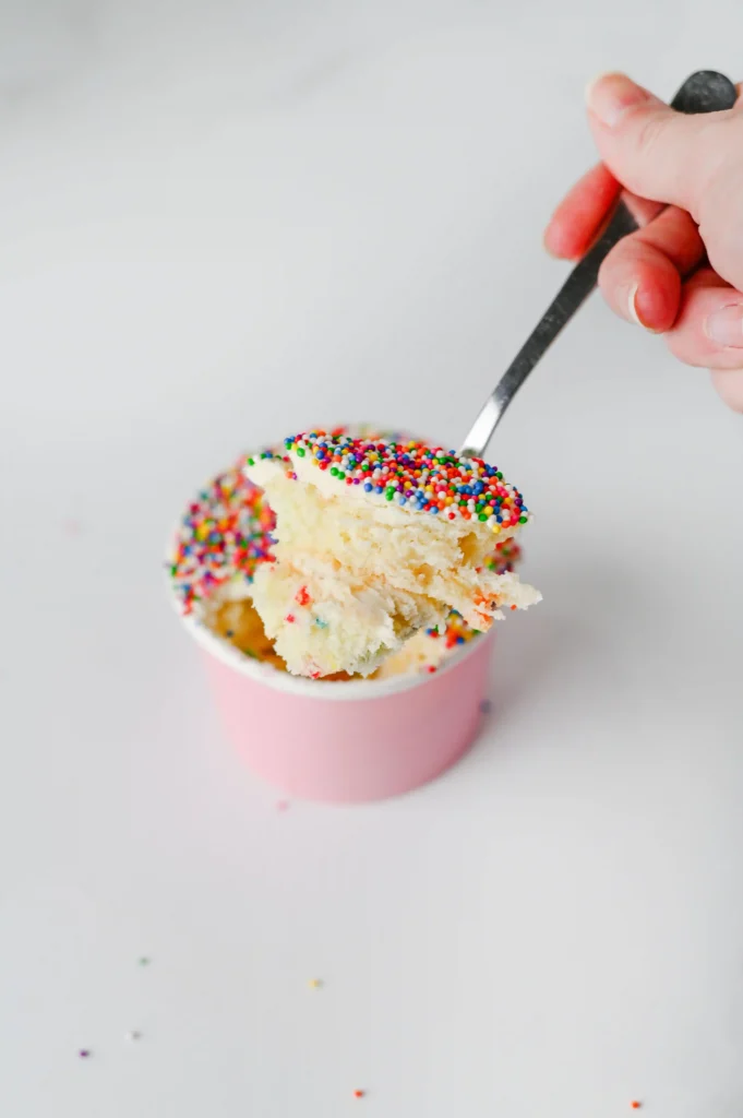 dot cakes in a paper cup with nonpareil sprinkles on top and a spoon scooping some out