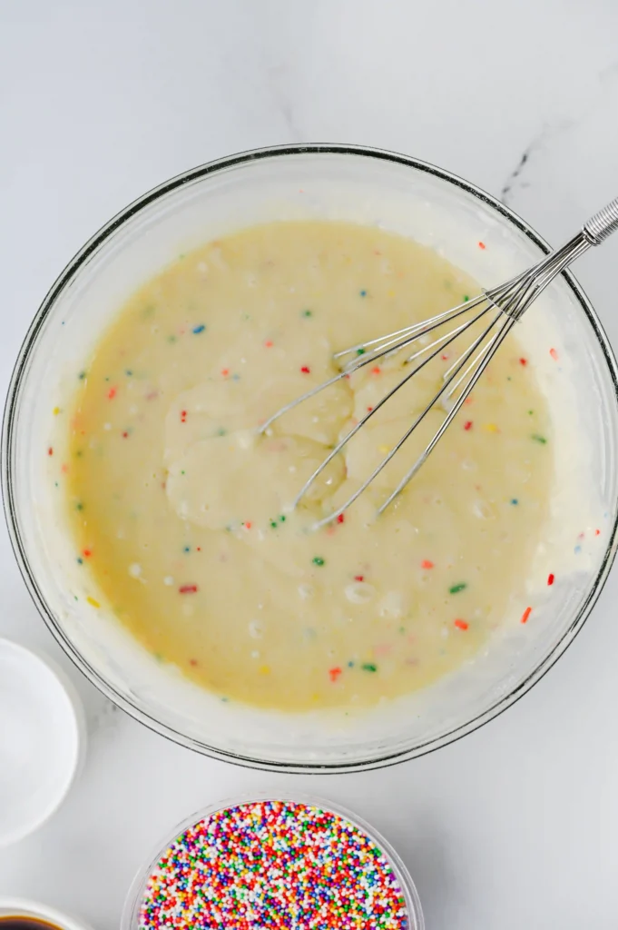 funfetti cake batter in a glass mixing bowl with a whisk