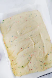 Unbaked funfetti cake dough with colorful rainbow sprinkles spread on parchment paper in a baking dish.