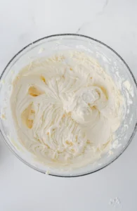 Top-down view of a glass bowl filled with fluffy white whipped frosting on a marble surface.