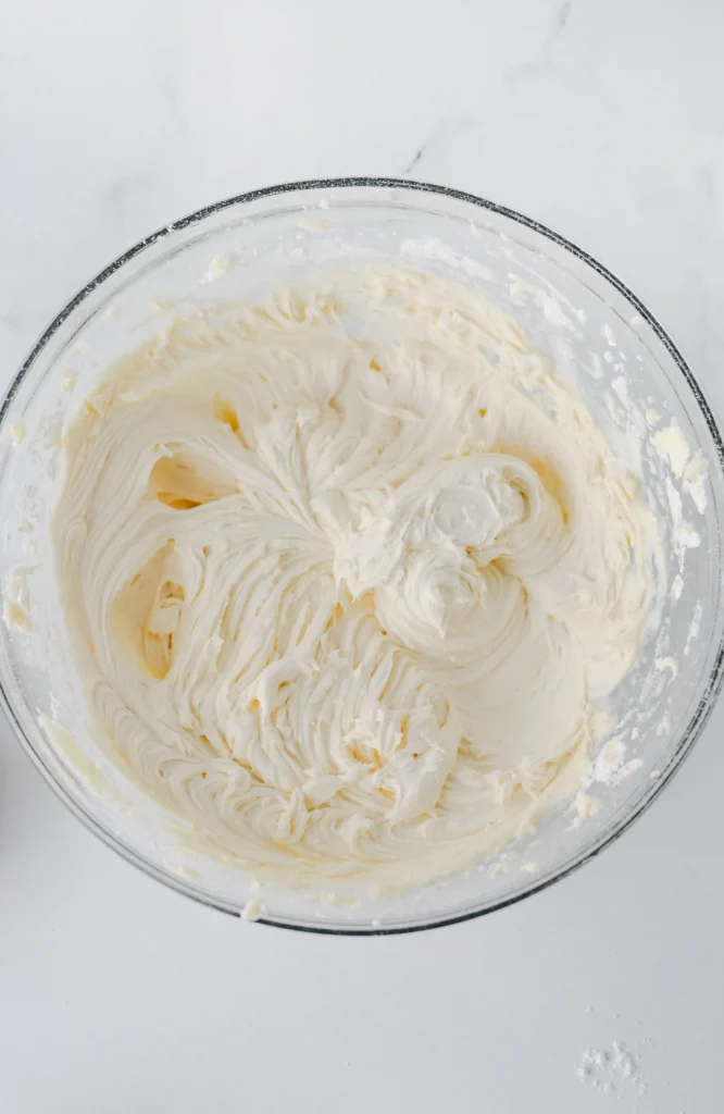 Top-down view of a glass bowl filled with fluffy white whipped frosting on a marble surface.