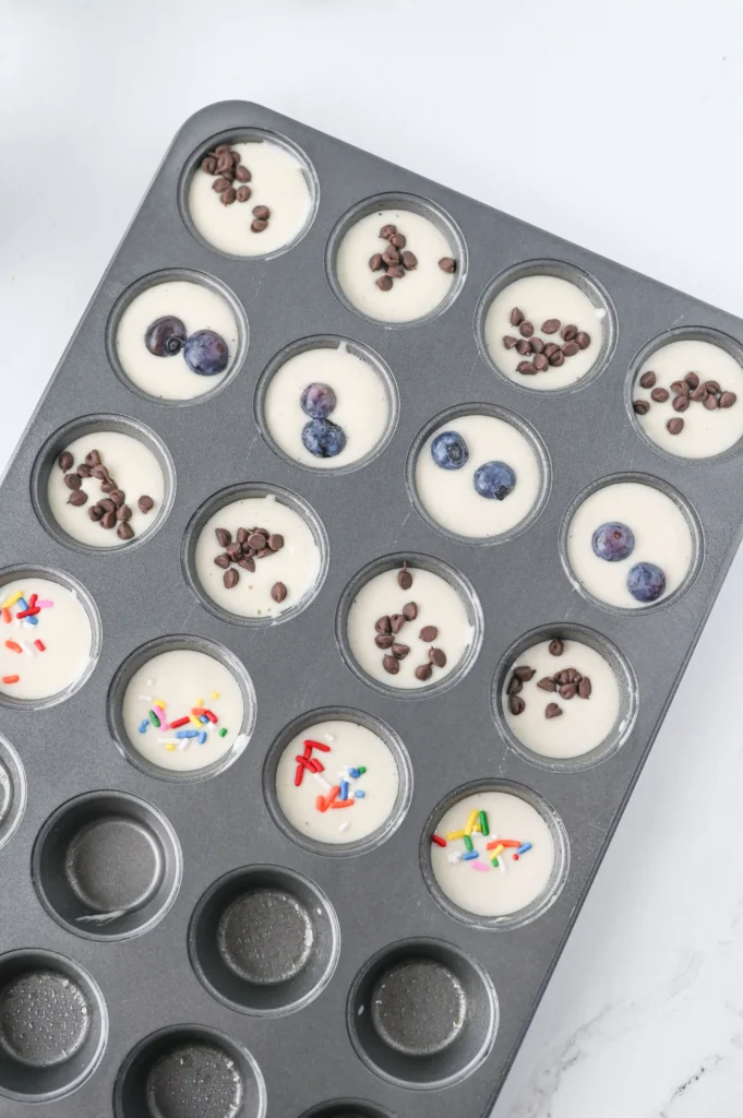 Muffin tin with unbaked pancake batter; some cups topped with blueberries and chocolate chips for  quick breakfast ideas