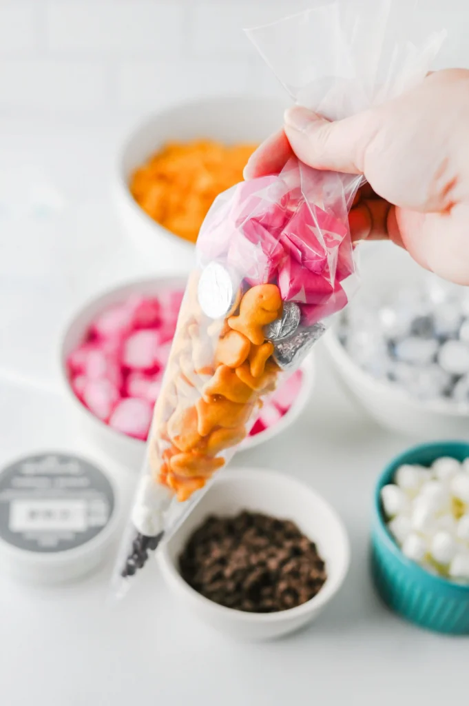 Close-up of a hand squeezing a clear plastic bag filled with snacks to resemble a pencil for these back to school party gifts