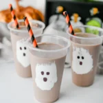 Chocolate Milk Ghost Cups that have marshmallow fluff ghosts in a cup with chocolate milk and an orange and black straw
