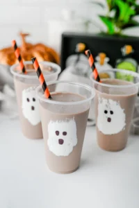 Chocolate Milk Ghost Cups that have marshmallow fluff ghosts in a cup with chocolate milk and an orange and black straw