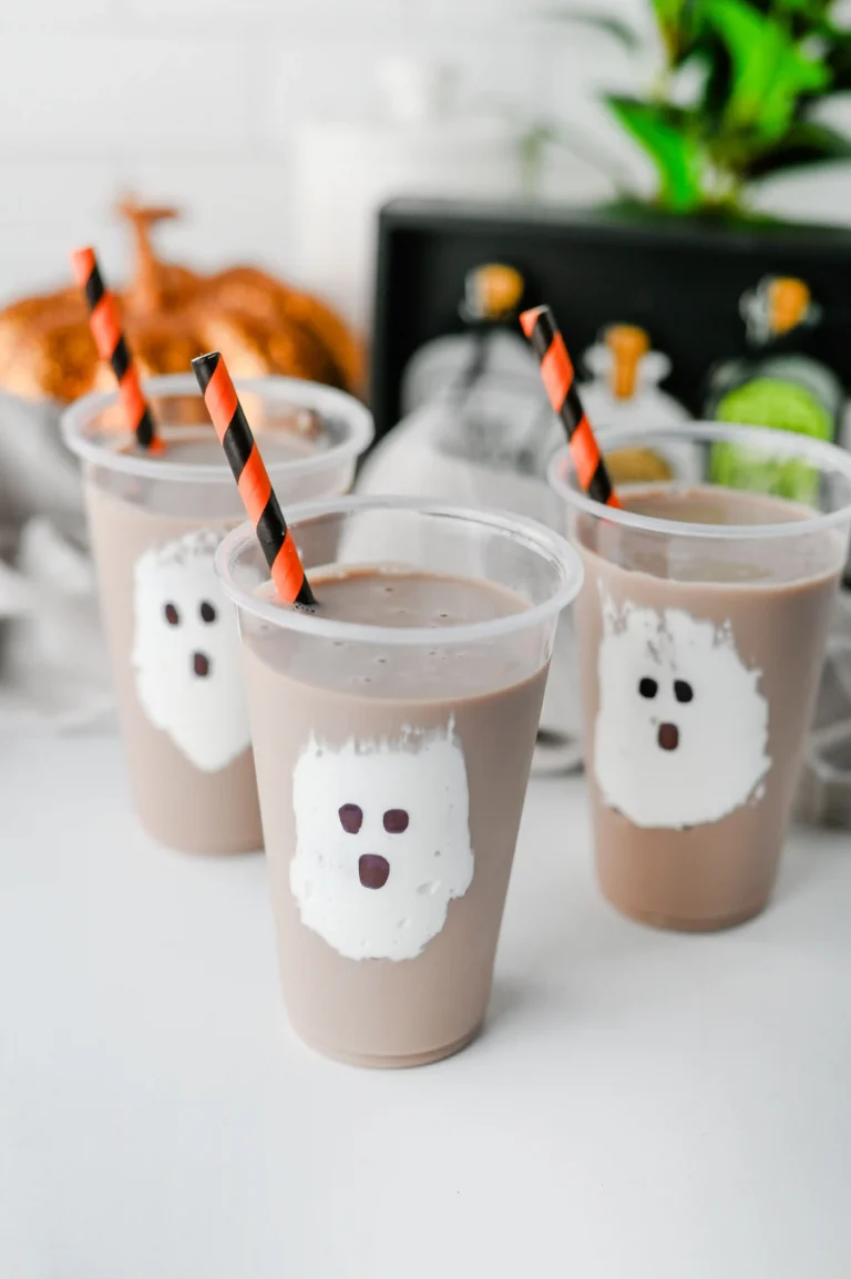 Chocolate Milk Ghost Cups that have marshmallow fluff ghosts in a cup with chocolate milk and an orange and black straw