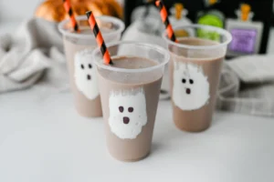 Chocolate Milk Ghost Cups that have marshmallow fluff ghosts in a cup with chocolate milk and an orange and black straw