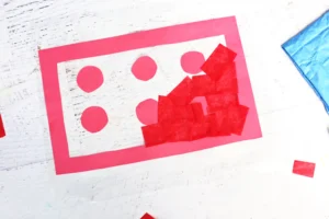 Close-up of a red-bordered with six red circular stickers and torn red paper shapes on a white wooden surface.