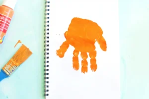Orange paint handprint on a white spiral notebook page for this alphabet craft for kids