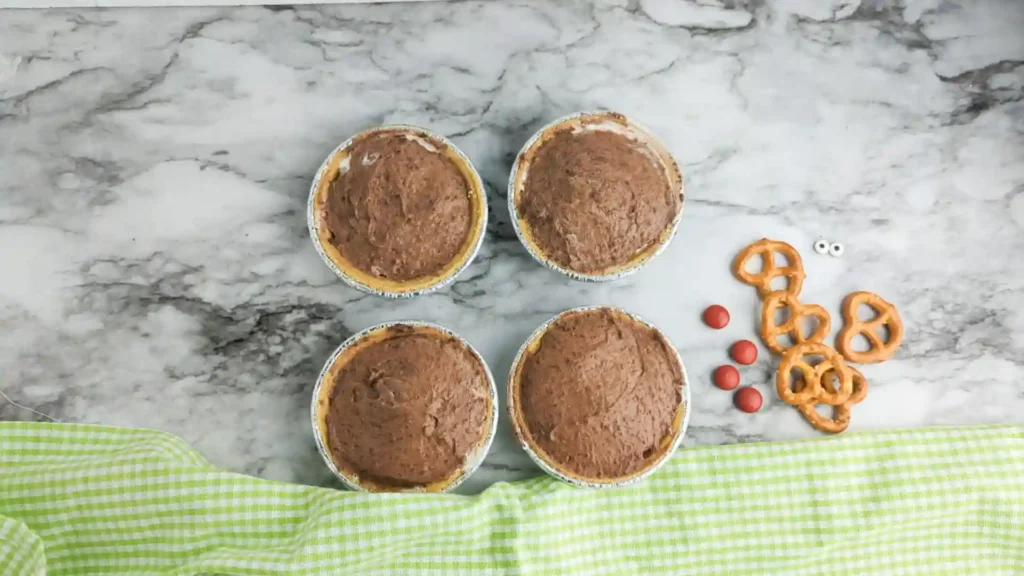 Mini Rudolph Pies - Cultivating Brilliant Minds Overhead shot of five round mini chocolate-pies on a marble countertop, with pretzels and red candies to the right.