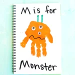 a letter m handprint craft that is an orange handprint decorated to look like a monster with the words "M is for monster" written on the page
