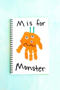 a letter m handprint craft that is an orange handprint decorated to look like a monster with the words "M is for monster" written on the page