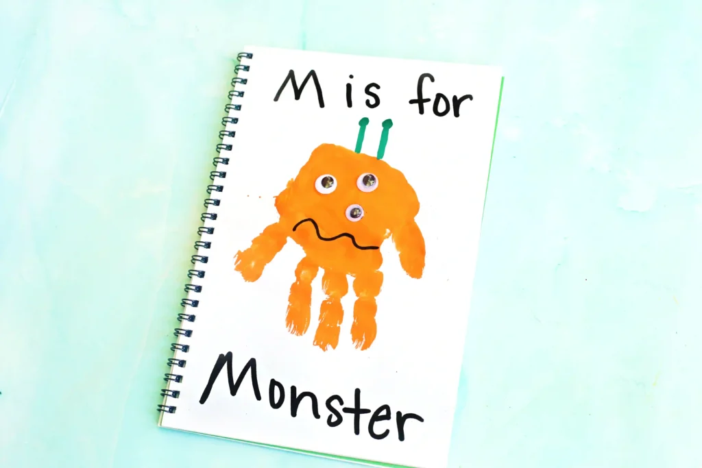 Letter M Handprint Craft - Cultivating Brilliant Minds Spiral notebook page with an orange monster drawing and the text'M is for' at top.