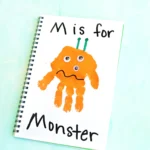 Spiral notebook page with an orange monster drawing and the text 'M is for' at top.