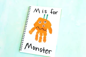 Spiral notebook page with an orange monster drawing and the text 'M is for' at top.