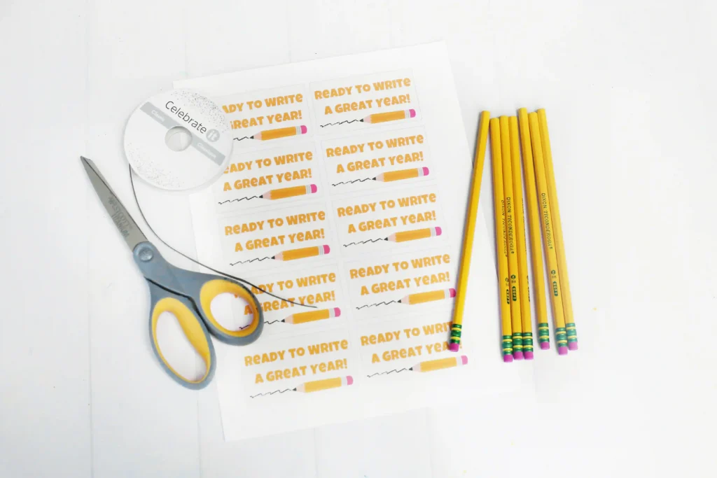 Desk scene with yellow pencils on the right, a pair of scissors on the left, and sticker sheets that read'Ready to write a great year!'