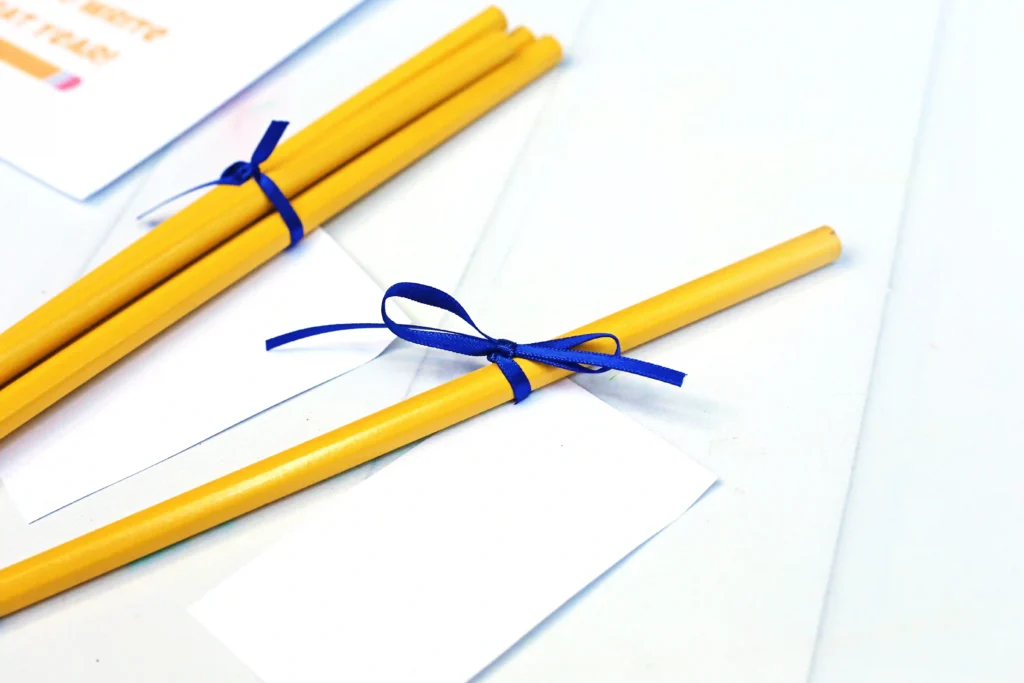 Yellow pencils tied with blue ribbons resting on white envelopes and papers, arranged diagonally on a bright surface.