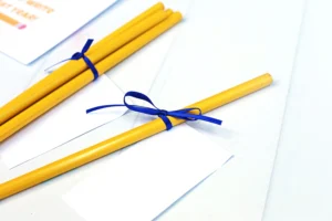 Yellow pencils tied with blue ribbons resting on white envelopes and papers, arranged diagonally on a bright surface.