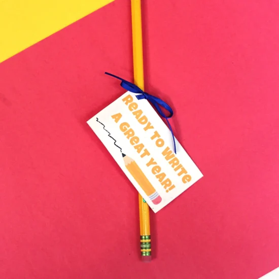 Yellow pencil with a tag that reads 'Ready to write a great year,' resting on a pink and yellow diagonal background.