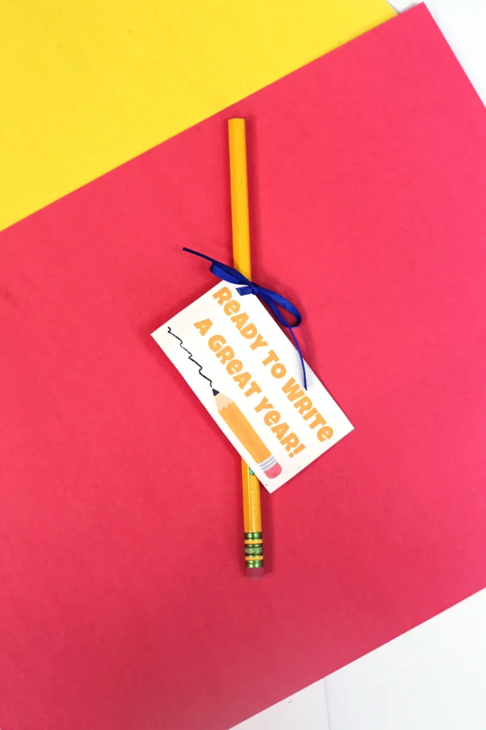 Yellow pencil with a tag that reads'Ready to write a great year,' resting on a pink and yellow diagonal background.