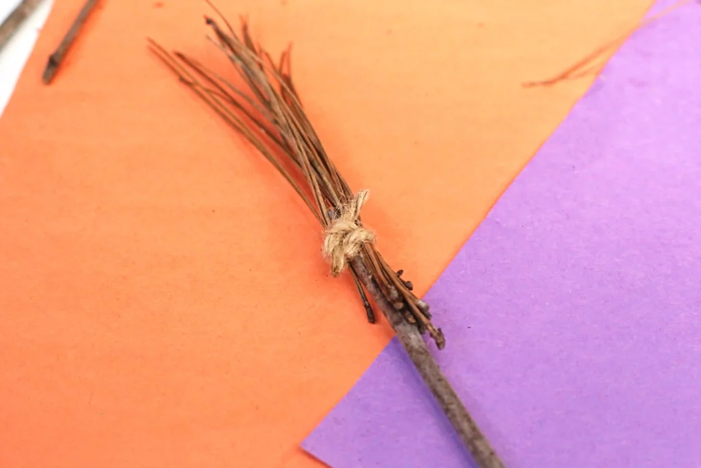 Bundle of thin brown twigs tied with jute twine on an orange and purple background