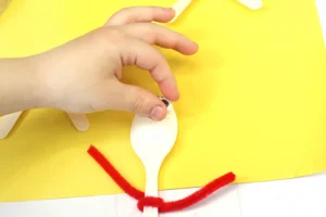 close up of a kid's hand gluing googly eyes on a spoon