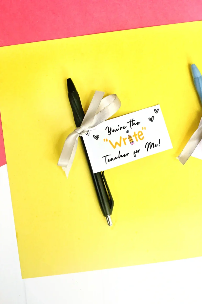 Pen with a white gift card reading "You're the Write teacher for Me!" on a bright yellow background, tied with a silver ribbon (teacher appreciation theme).