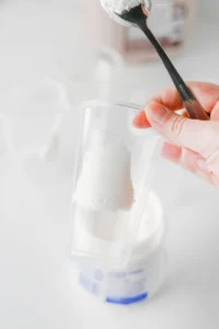 a hold holding a metal spoon and a cup that has a smear of marshamllow fluff on the inside for these halloween drink ideas