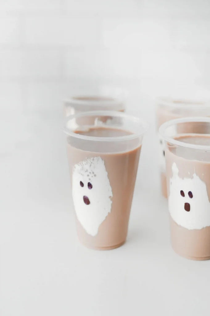Chocolate Milk Ghost Cups that have marshmallow fluff ghosts in a cup with chocolate milk
