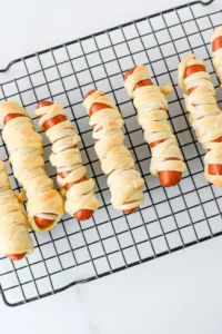 hot dogs wrapped in pale pastry laid on a metal cooling rack for a halloween lunch