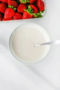 Strawberries in a clear plastic container beside a bowl of melted vanilla almond bark for this healthy halloween treat
