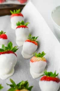 Strawberries dipped in white chocolate with green leaves on parchment paper for these halloween party snacks