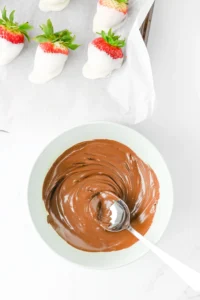 Strawberries dipped in white chocolate arranged on parchment with a bowl of melted chocolate in the foreground for these ghost snacks for halloween
