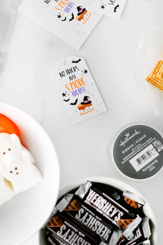 Halloween S'mores Treat Bags - Cultivating Brilliant Minds Halloween-themed tag reads 'No Tricks Just S’more Treats' with a witch hat and bats on a white card atop a light background.