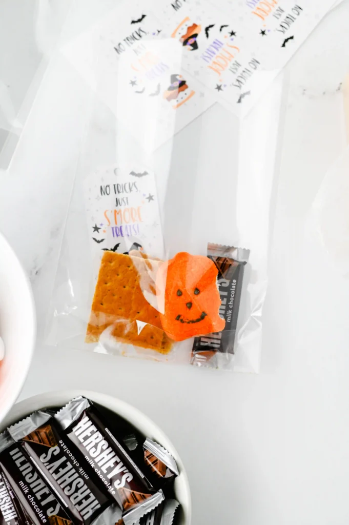 Halloween S'mores Treat Bags - Cultivating Brilliant Minds Halloween-themed bag with orange jack-o'-lantern peep and Hershey's chocolate bars inside a white wrapper.