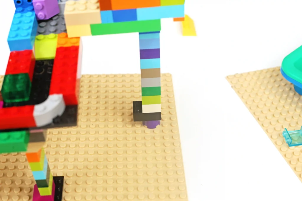 Close-up of a colorful LEGO construction with rainbow bricks on a beige baseplate.